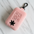 Pink fuzzy pouch with black clasp and embroidered symbols on marble background